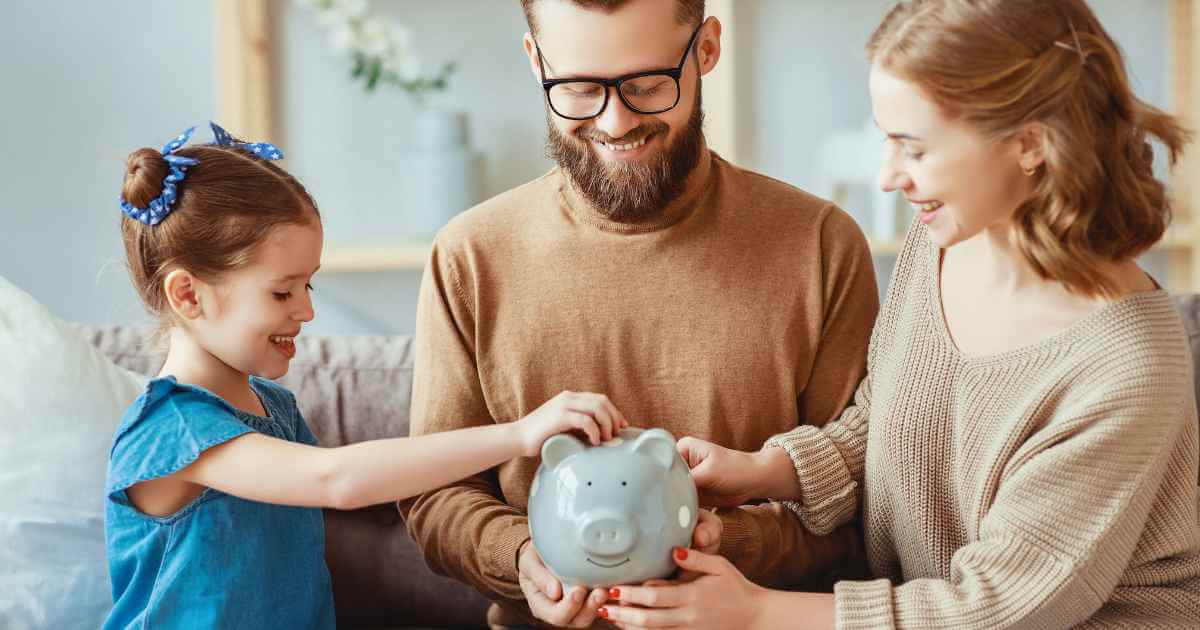 a man and his wife holding a piggy bank for their daughter to drop in coins for their budgeting plan