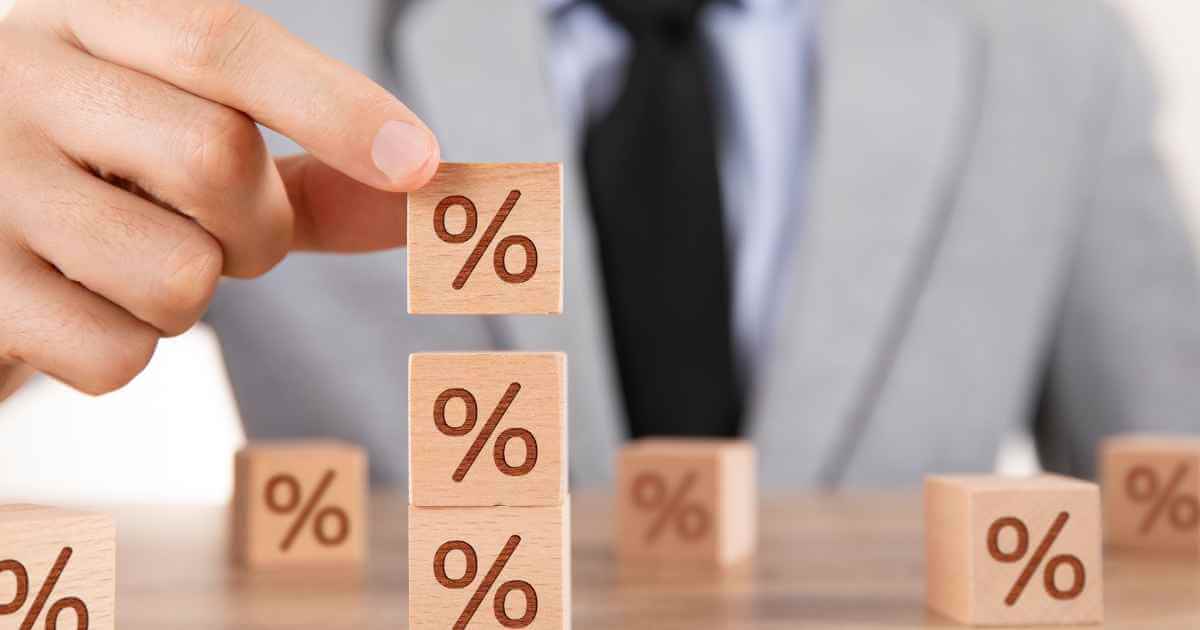 a man stacking wood blocks with a % symbol depicting high car interest rates