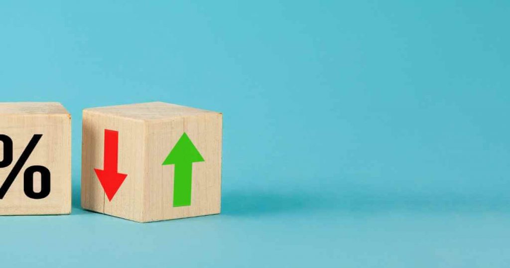 two wood blocks with one that has a % symbol on it and the other a red arrow down and green arrow up representing interest rates