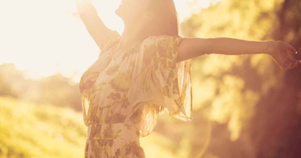 a woman stretching her arms out in the sun embracing the world around her