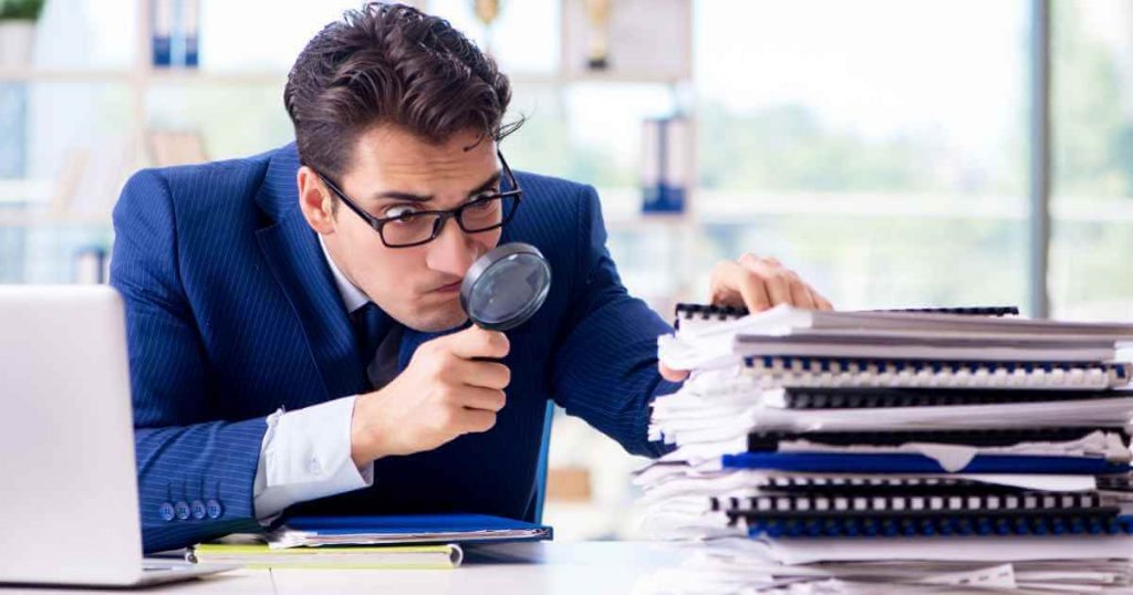 a man with a magnifying glass inspecting a stack of papers representing what in house financing dealerships look for