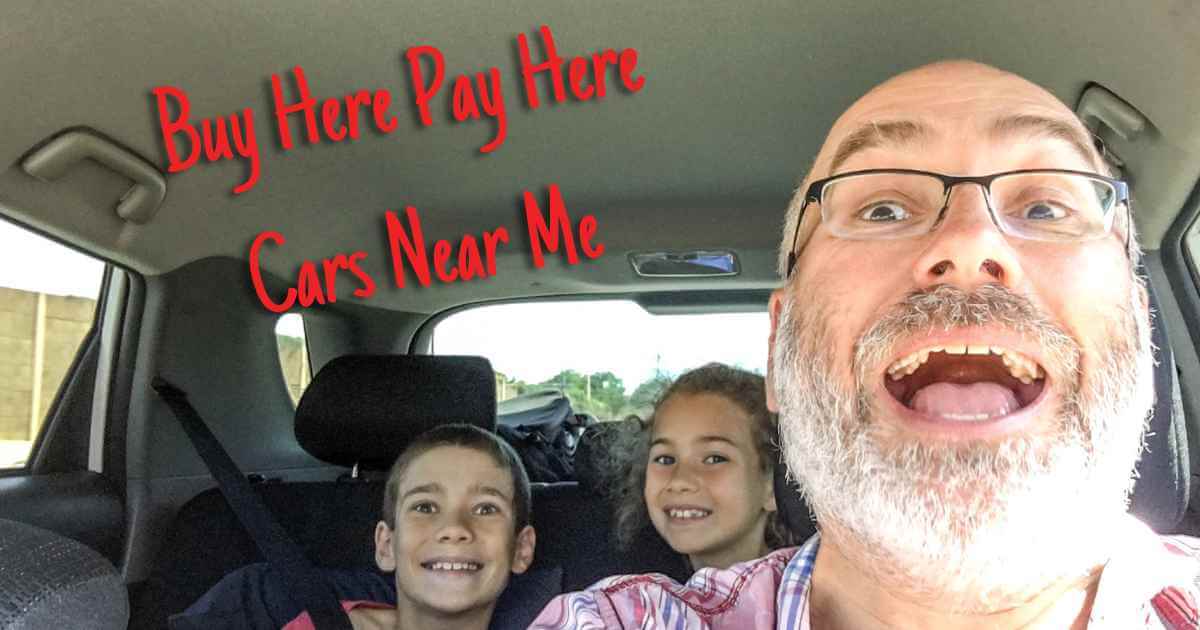 a man in a car with his young kids smiling gleefully and the words buy here pay here cars near me over them