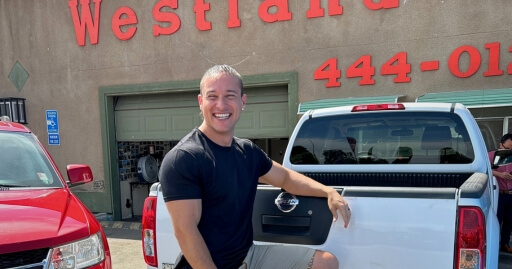 A staff member of Westland Auto Sales - buy here pay here leaning against a truck and laughing gleefully. 