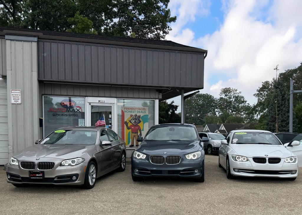 Used BMW for Sale in Mishawaka at Automax Indiana — lineup of BMW sedans parked in front of the dealership with Automax mascot sign.