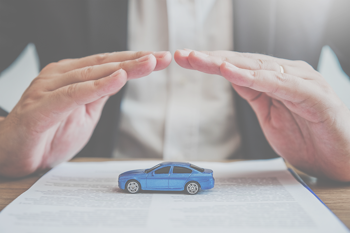 Hands protecting a small blue car on paperwork, symbolizing auto warranty and coverage.